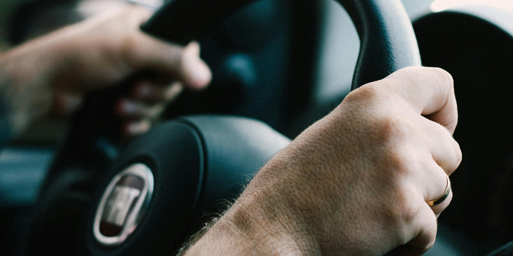 Close up of a man driving a car with hands at 10 and 2.